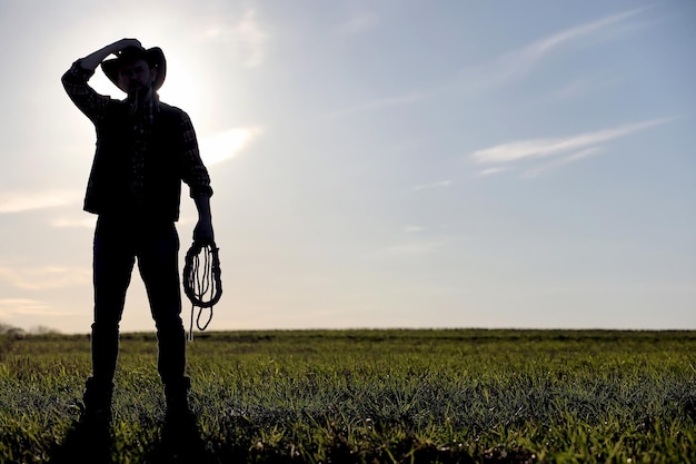 A man cowboy hat and a loso in the field American farmer in a field wearing a jeans hat and with a loso A man is walking across the field silhouette