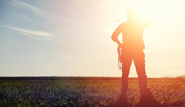 A man cowboy hat and a loso in the field American farmer in a field wearing a jeans hat and with a loso A man is walking across the field silhouette