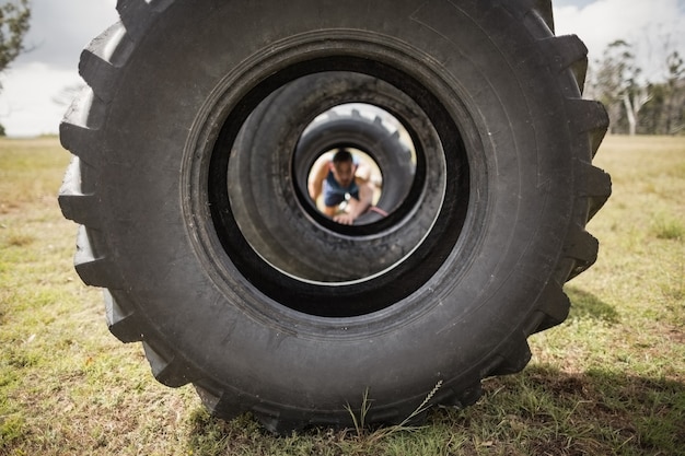 Photo man crawling through the tire during obstacle course in boot camp