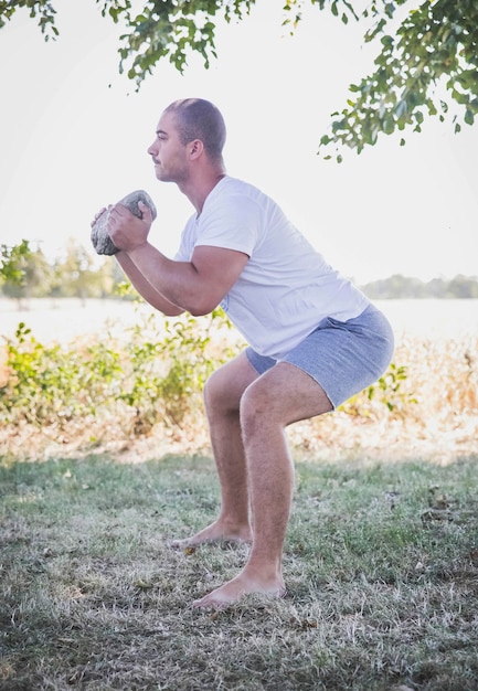 man crouches in the garden with a stone in his hands