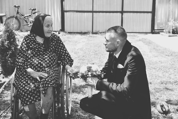 Photo man crouching by mother sitting on wheelchair in yard