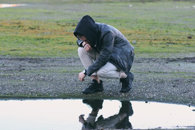 Photo man crouching at puddle on field