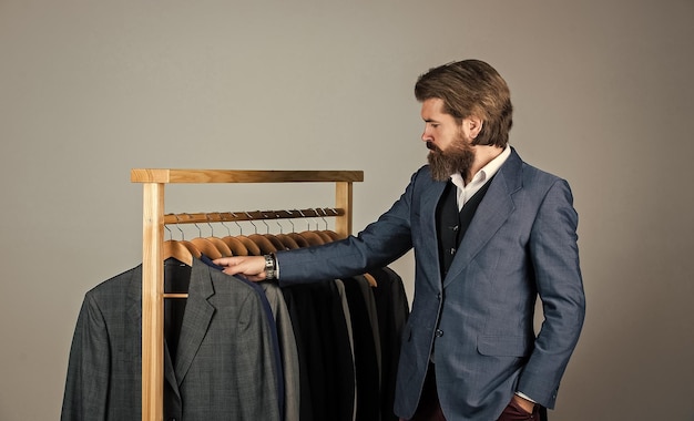 Man in custom tailored suit presenting expensive tailored\
tuxedo man clothing in boutique man with suit tailor in his\
workshop handsome bearded fashion man in classical costume\
suit