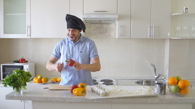 The man cuts the bell pepper in the kitchen.