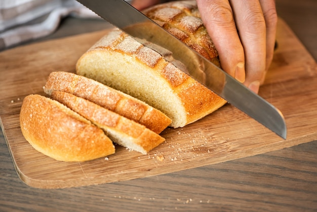 Un uomo taglia il pane con un coltello seghettato.