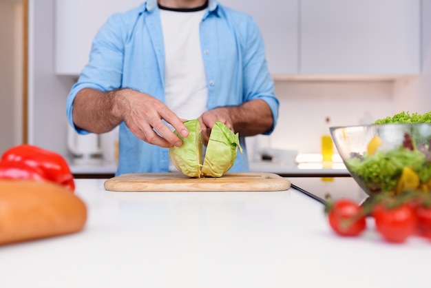 Man cuts the cabbage with a knife on a wooden board at the kitchen