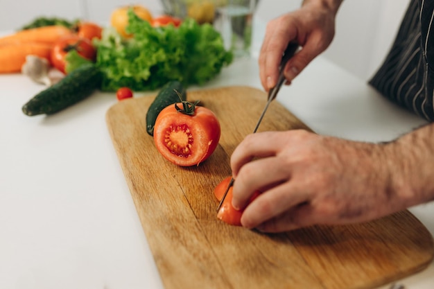 A man cuts a red tomato on a board