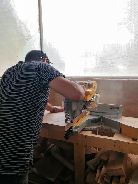 A man cuts wood on a circular saw in a joinery band saw holding\
a plank