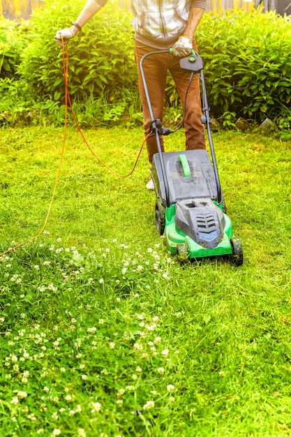 Uomo che taglia erba verde con tosaerba in cortile. fondo di stile di vita del paese di giardinaggio.