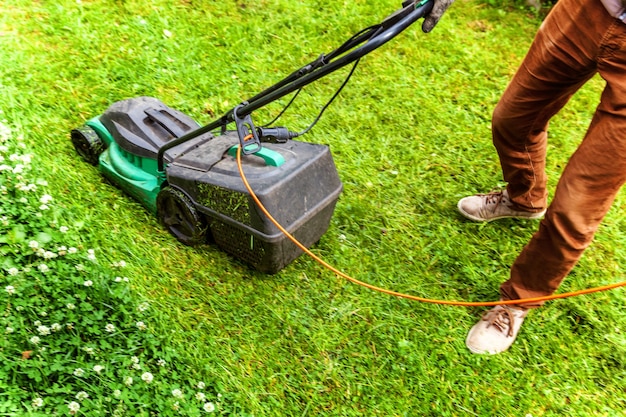 Man cutting green grass with lawn mower in backyard. Gardening country lifestyle background.