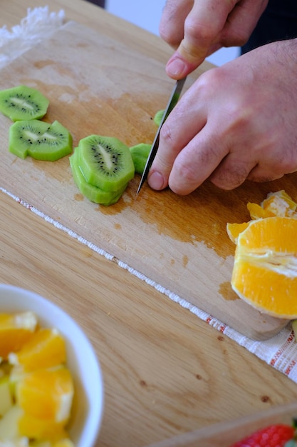 Foto uomo che taglia il kiwi su una tavola da taglio di legno