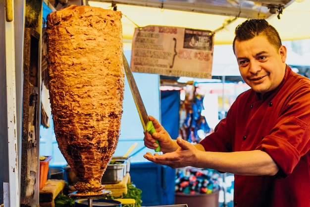 Uomo che taglia pezzi di un pezzo di carne in una trottola per tacos al pastor, piatto tipico messicano.