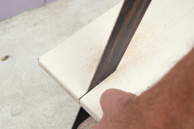 Man cutting through wooden board with hand saw in garden