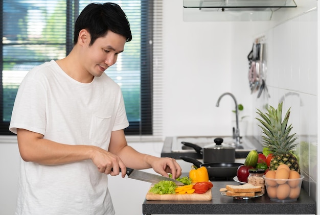 自宅のキッチンで健康的な食品を準備するために野菜を切る男