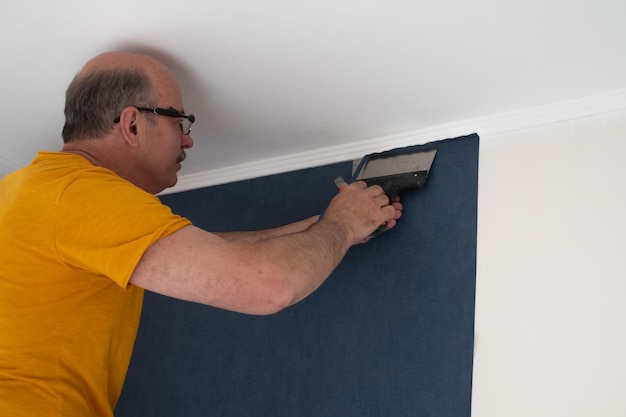 Man cutting wallpaper. Maintenance repair works renovation in the flat. Restoration indoors.