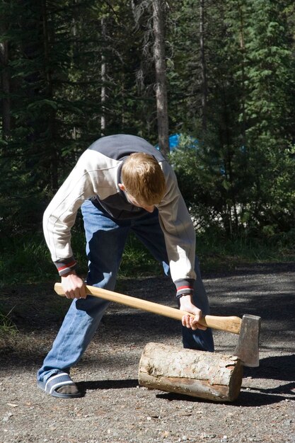 Foto uomo che taglia un tronco di legno mentre è in piedi sulla strada