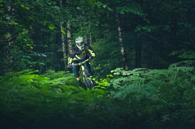 Man, cyclist in the full face helmet fast rides on the yellow enduro bicycle in the green forest
