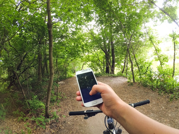 A man cyclist stands in the forest on a dirt road with a bicycle and holds a telphone in his hand