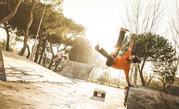 Foto man dansen met mannelijke vriend fietsen op skateboard park tijdens zonsondergang