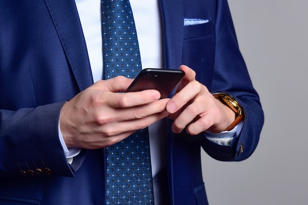 Man in a dark blue suit checks messages on his phone.