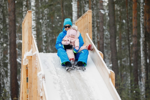 Man and daughter slide down an icy wooden hill on a snowy day.