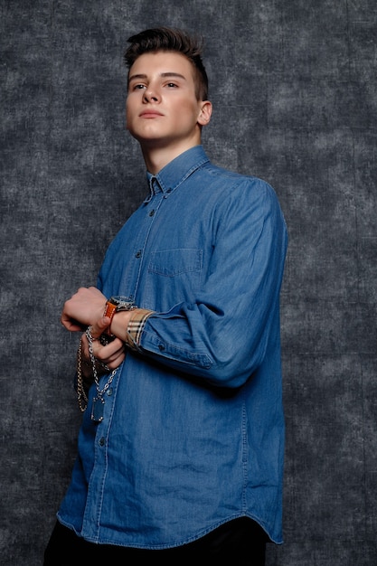 Man in denim shirt, arms on hips, gray background. People lifestyle concept. Mock up copy space. Straightening sleeves looking aside