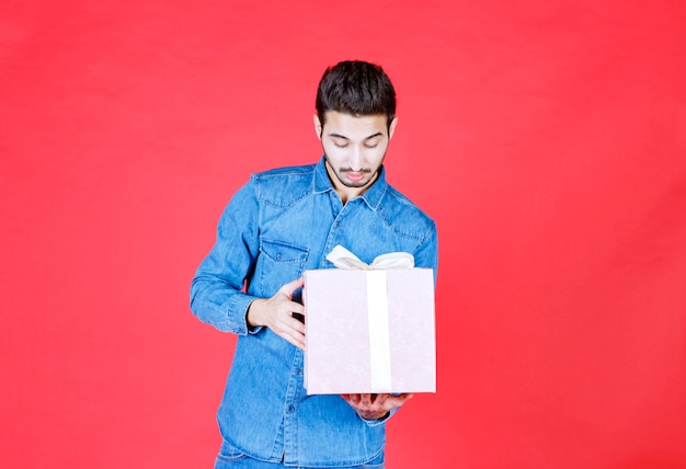 Man in denim shirt holding a purple gift box tied with white ribbon.