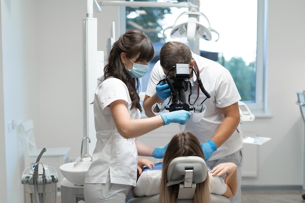 Photo a man dentist at work and a nurse treating the teeth of a woman sitting in a chair. orthodontists are engaged in prosthetics. copy space. oral medicine and health concept.