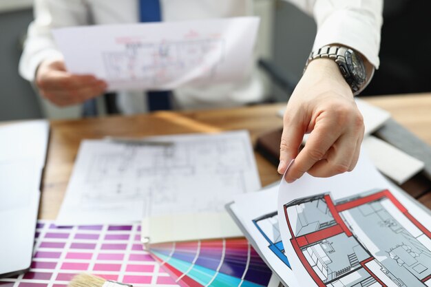 Photo man designer sitting at table and holding design project of apartment in his hands