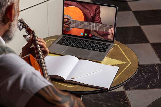 Man die akoestische gitaar speelt en online lessen op laptop bekijkt terwijl hij thuis oefent... Online training, online lessen.