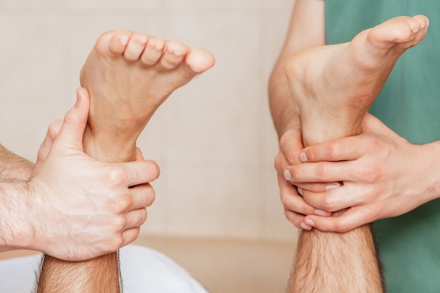 Man die beenmassage op zijn voeten ontvangt door twee massagetherapeuten, close-up.