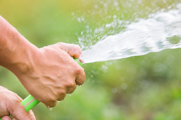 Man die de tuin op zonnige dag uit de slang water geeft