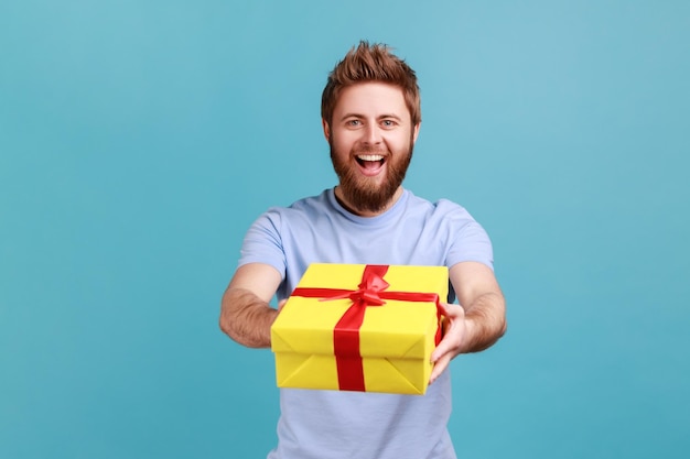 Man die een geschenkdoos met rood lint aan de camera geeft en lacht om een vakantiecadeau te delen feliciteren