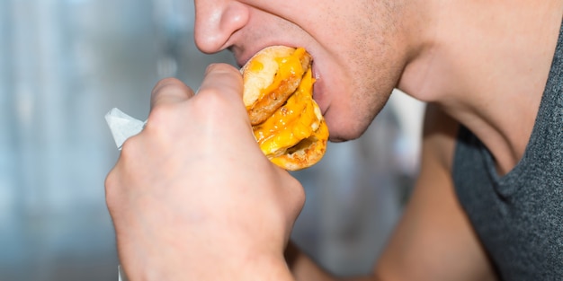 Man die een grote hamburger eet met een kotelet, kaas en gebakken eieren, close-up.