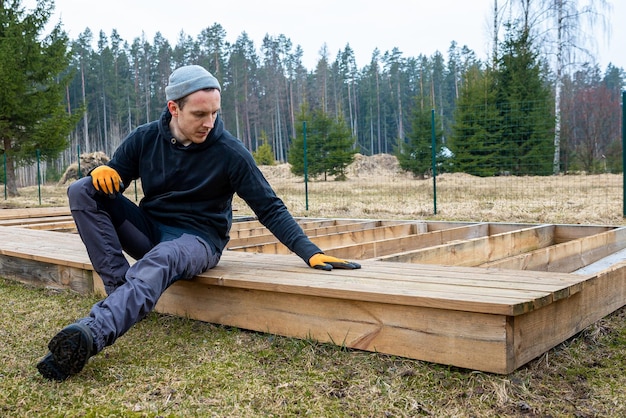 man die een houten dek of terras bouwt in een plattelandse buitenomgeving die DIY-snijderijvaardigheden en huisverbeteringen toont