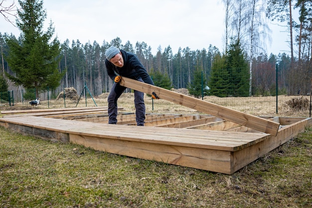 man die een houten dek of terras bouwt in een plattelandse buitenomgeving die DIY-snijderijvaardigheden en huisverbeteringen toont