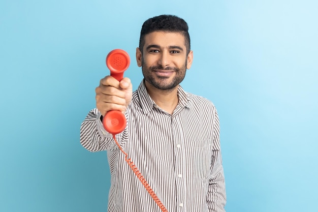 Man die een telefoontoestel geeft en naar de camera kijkt die lacht en er vriendelijk uitziet, vrolijk behulpzaam contactcenter