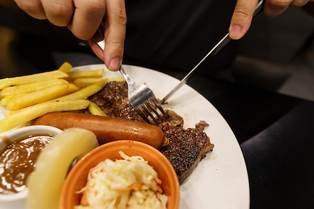 Man die gegrild vlees eet, paal van bord, hand met mes en vork, gegrilde biefstuk snijden