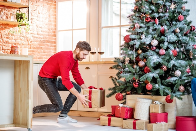 Man die geschenken onder de kerstboom legt en zich voorbereidt op een nieuwjaarsvakantie thuis