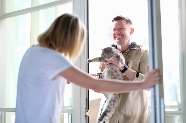 Foto man die grijze kat aan vrouw geeft via de deur. overmatige blootstelling van huisdierenconcept