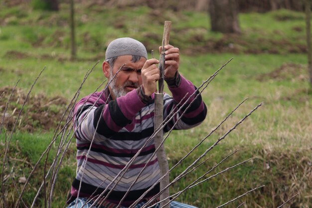 Foto man die hout snijdt met gereedschap terwijl hij op het gras zit