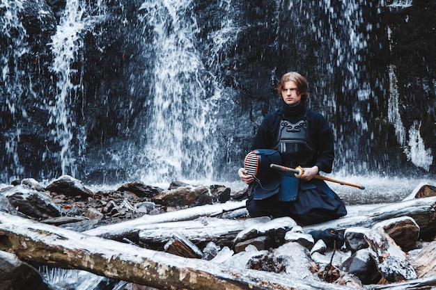 Man die kendo beoefent met bamboezwaard op watervalachtergrond