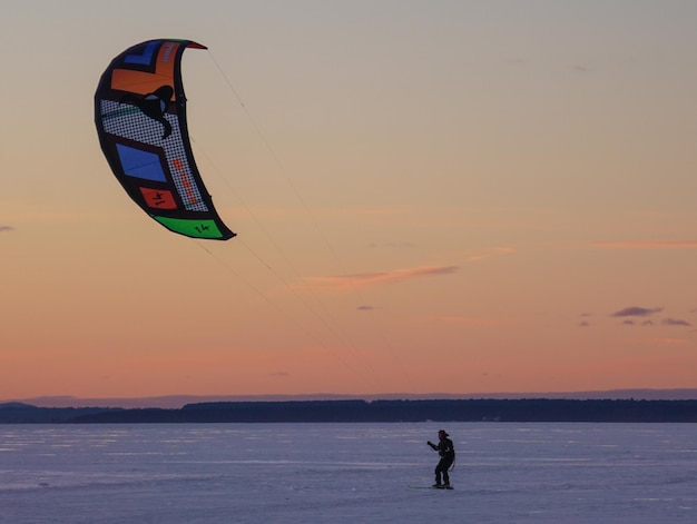 Foto man die kitesurft op een met sneeuw bedekt veld bij zonsondergang