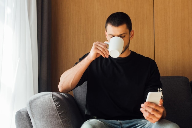 man die koffie drinkt en een smartphone gebruikt in de woonkamer