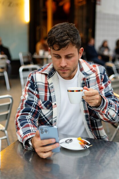 Man die koffie drinkt en smartphone doorbladert in straatcafé
