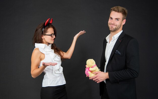 Man die met Valentijnsbeer voorstelt aan boos meisje in rode duivelshoorns donkere achtergrond Halloween