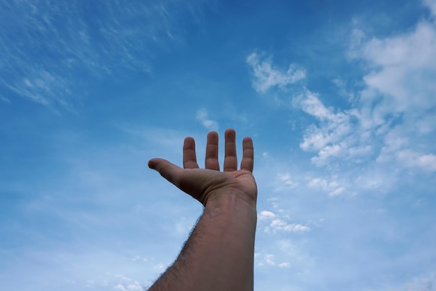man die met zijn hand naar de blauwe hemel reikte