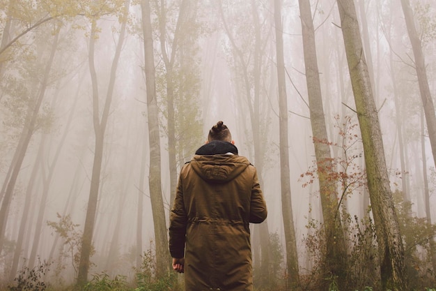 Foto man die midden in de bomen staat tijdens mistig weer