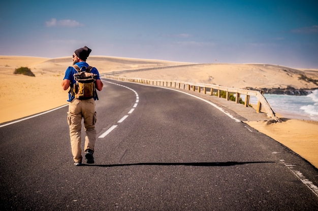 Man die midden op een lange weg loopt met woestijn aan beide kanten en oceaanstrand