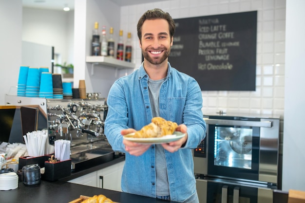 Man die naar camera kijkt die croissant op plaat aanbiedt